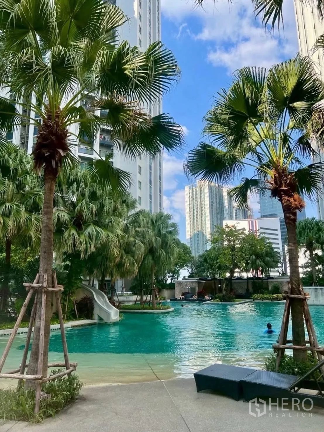 Condominium for rent in Huai Khwang, Bangkok - Resort-style swimming pool with slide, palm trees, and deck.