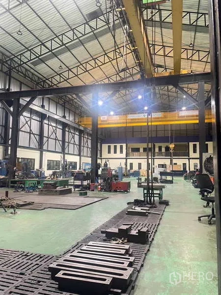 工厂 出售在Si Racha, Chon Buri - 夜间厂房内景，重型钢柱、行车与工位照明明亮。
