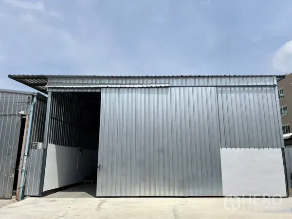 货栈 出租在Saphan Sung, Bangkok - 仓库外观，金属板立面与大型推拉门，前方混凝土场地，天空晴朗，位于曼谷沙攀颂区