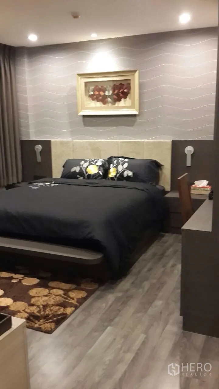 Condominium for rent in Mueang Samut Prakan, Samut Prakan - Cozy bedroom with king bed, soft ceiling lights, wood flooring, and a built-in desk with framed artwork on the feature wall.