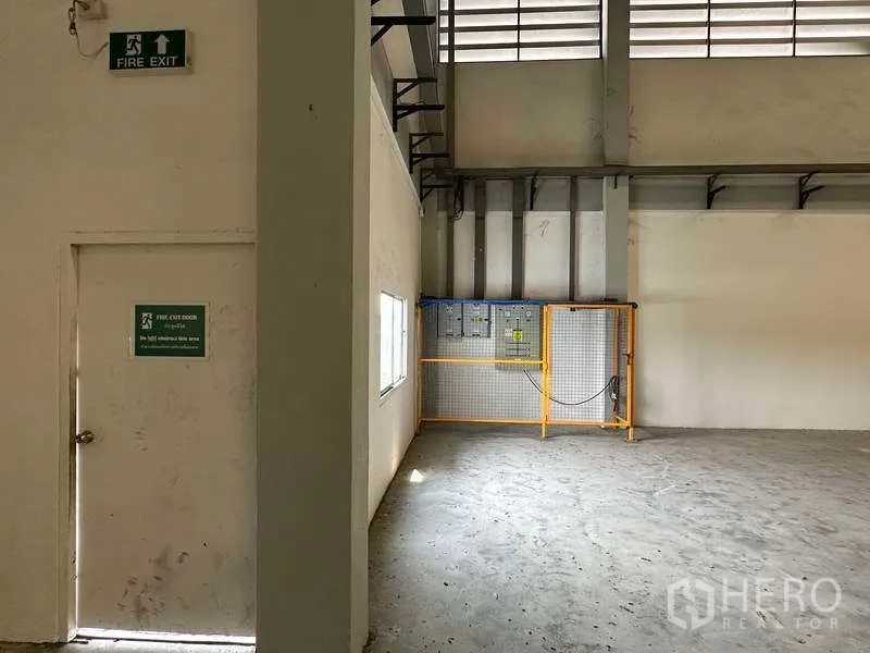 Warehouse for rent in Samut Prakan - Warehouse corner with fire exit door and fenced electrical control panel.