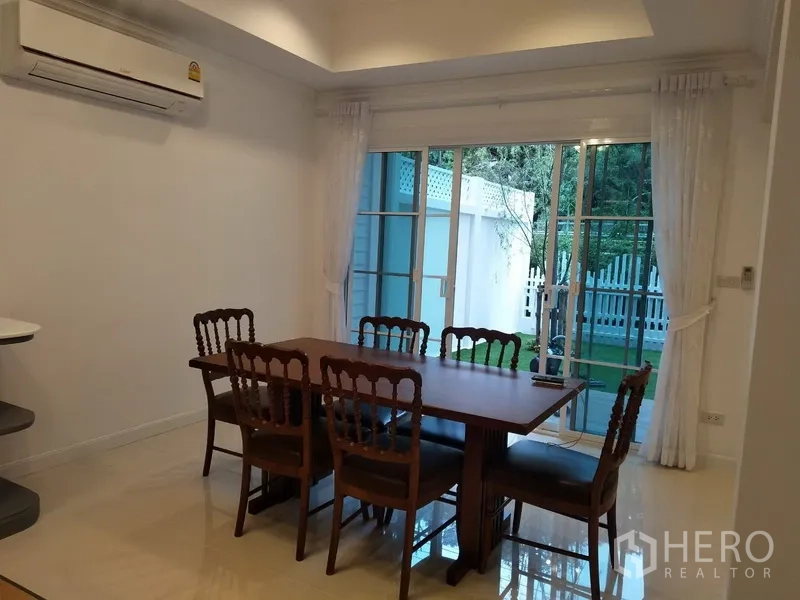 联排别墅 出租在Mueang Samut Prakan, Samut Prakan - 采光良好的餐厅，木质餐桌，推拉落地门通向花园。