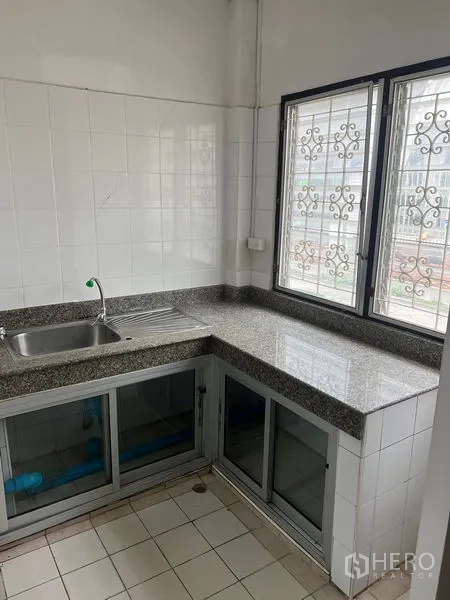 Townhouse for rent in Khlong Toei, Bangkok - Compact L-shaped kitchen with granite countertops, sink and grilled windows.