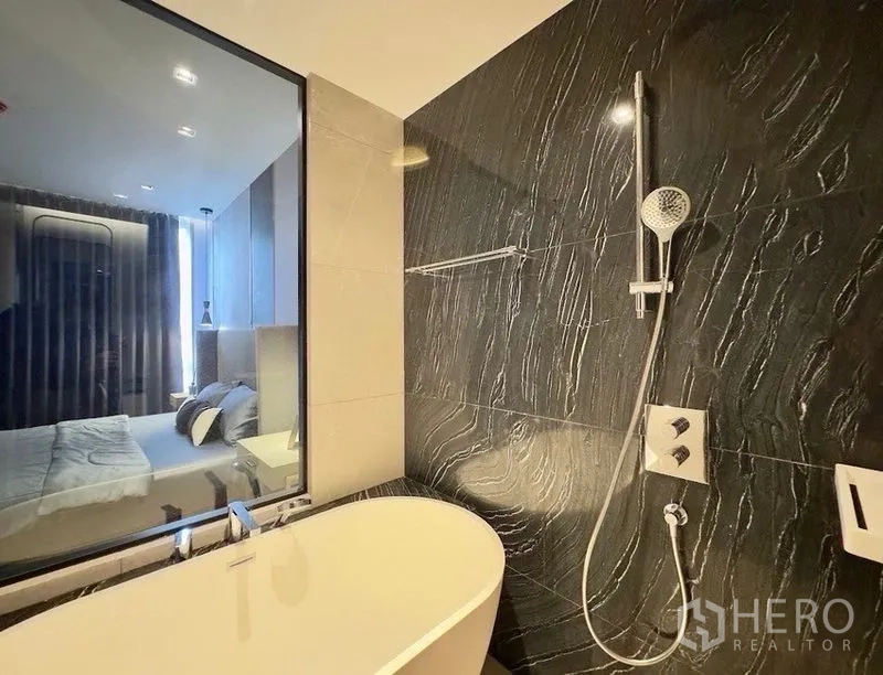 公寓 for rent or sale in Watthana, Bangkok - 浴室设独立式浴缸，窗旁布局，深色墙面配壁挂式淋浴。