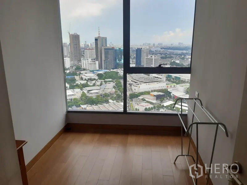 Condominium for rent in Khlong Toei, Bangkok - High-rise city view through floor-to-ceiling windows from a bedroom or study.
