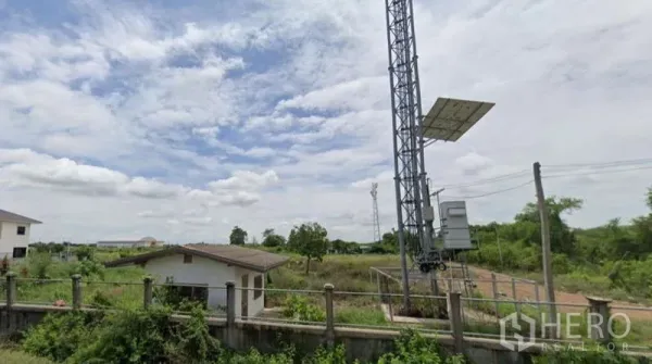 Land for sale in Bang Sao Thong, Samut Prakan - Fenced corner of the land with a small utility house and cell tower, indicating power and telecom on site.