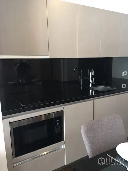 Condominium for rent in Watthana, Bangkok - Compact kitchen with black backsplash, induction hob, sink and built-in microwave.