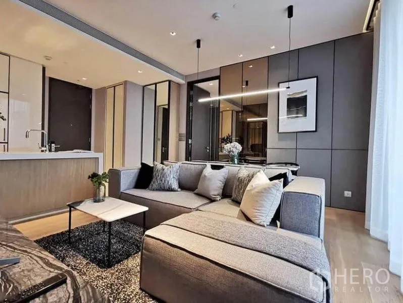 คอนโด ให้เช่าในKhlong Toei, Bangkok - โซฟารูปตัวแอลกับไฟห้อยและผนังกระจกเงา เห็นเคาน์เตอร์ครัวด้านหลัง