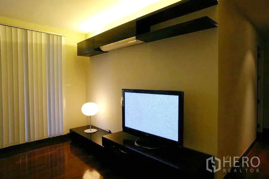 公寓 出租在Watthana, Bangkok - 电视角落，竖百叶窗，带LED灯的搁架，矮柜与圆形台灯。