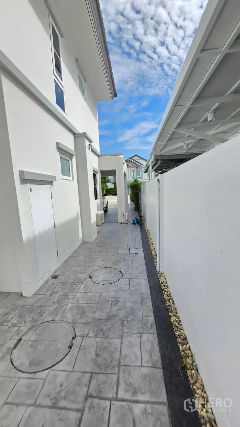 Detached House for rent in Bang Phli, Samut Prakan - Side walkway of a white detached house with patterned tiles and a covered area.