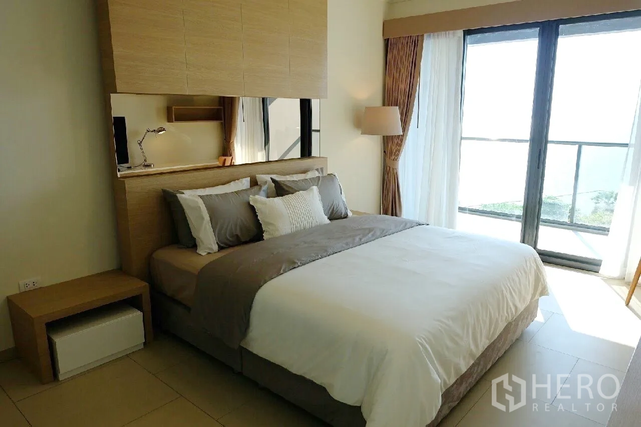 Condominium for rent or sale in Bang Lamung, Chon Buri - Bright bedroom with king bed, built-in headboard and floor-to-ceiling windows to a sea-view balcony.
