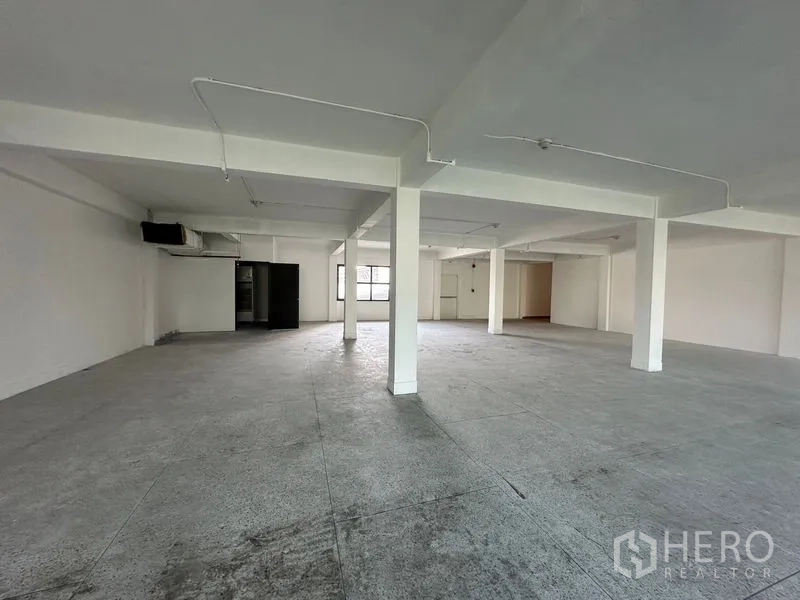 Office Space for rent in Khlong Toei, Bangkok - Open-plan office floor with white columns, exposed conduit lighting and durable concrete flooring.