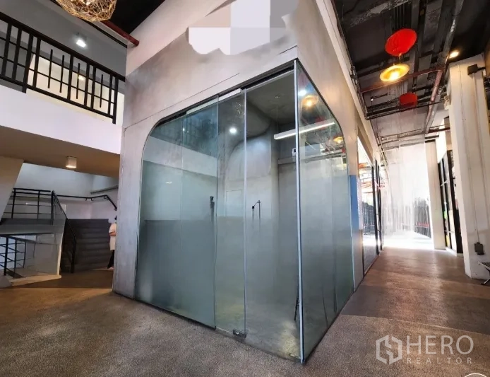 Retail Space for rent in Sathon, Bangkok - Corner glass-walled retail kiosk along a bright corridor with exposed ceiling lights and a nearby staircase and mezzanine.