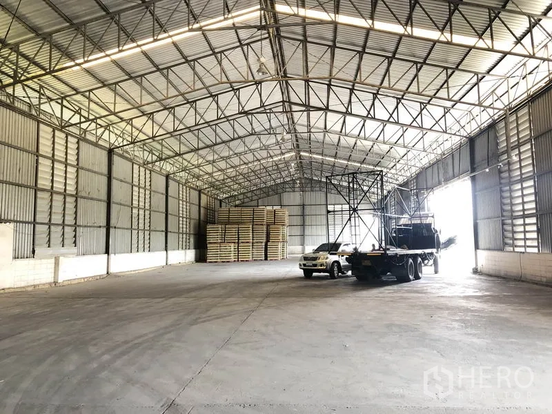 คลังสินค้า ให้เช่าในPathum Thani - ภายในโกดังโล่งสูง 8 เมตร พื้นคอนกรีต มีโครงหลังคาเหล็กและรถบรรทุกจอด