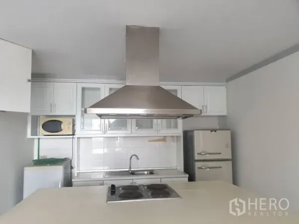 Condominium for rent in Watthana, Bangkok - Separate kitchen with stainless range hood, electric cooktop, sink, and fridge.