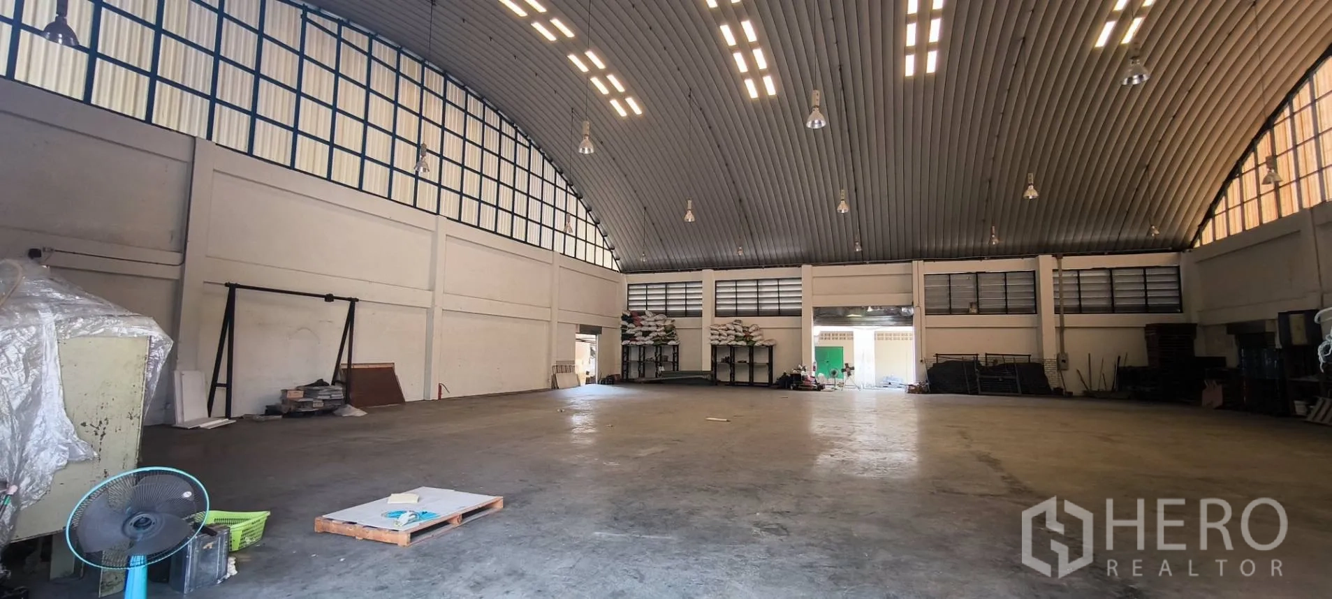 Warehouse for rent in Photharam, Ratchaburi - Open warehouse hall showing high bay lights, louvered vents, and side loading door.