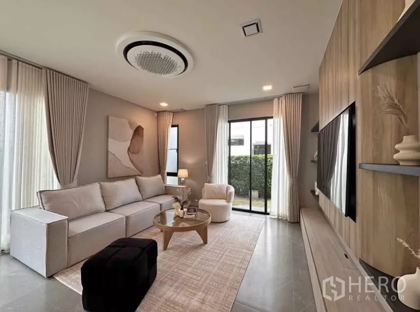 Detached House for rent in Samut Prakan - Bright living room with large sofa, full-height curtains, and sliding glass doors to the garden.