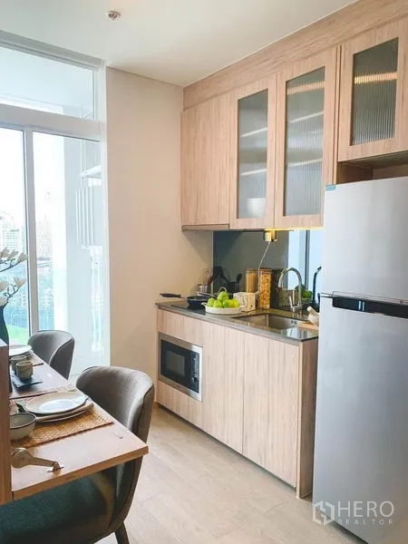 คอนโด ขายในKhlong Toei, Bangkok - ครัวขนาดกะทัดรัด ตู้ไม้โทนอ่อน อ่างล้างจาน ไมโครเวฟ และตู้เย็นข้างหน้าต่าง