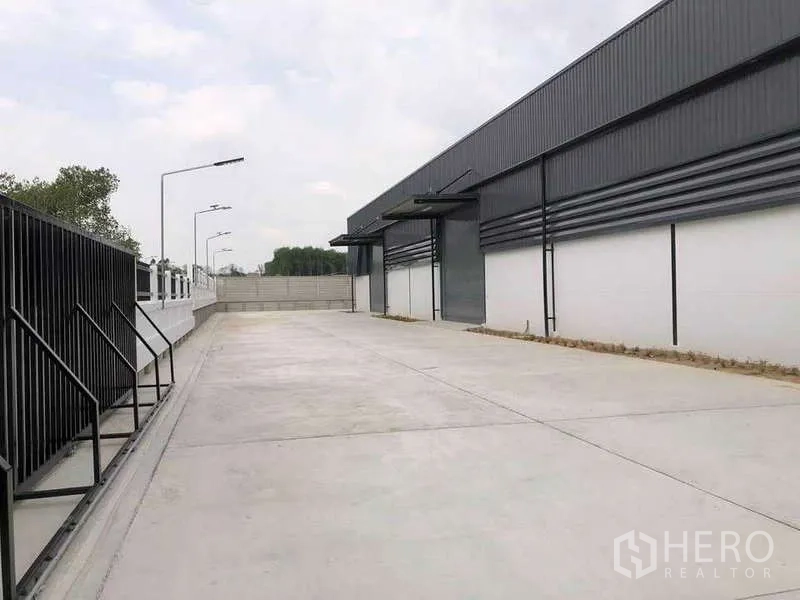 คลังสินค้า ให้เช่าหรือขายในNikhom Phatthana, Rayong - ลานคอนกรีตกว้างข้างโกดังสีเทาทันสมัย พร้อมประตูม้วนและไฟถนน ในนิคมพัฒนา ระยอง