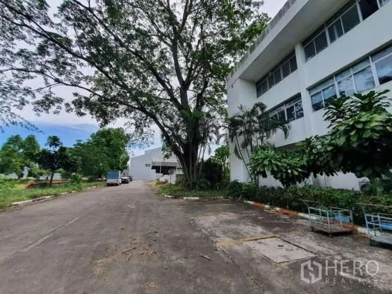工厂 出售在Rayong - 树荫大道旁的白色办公楼，配长条窗，通往后方仓储与厂区。