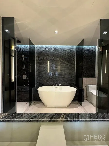 Condominium for rent in Watthana, Bangkok - Luxurious bathroom with freestanding soaking tub and dark stone wall.