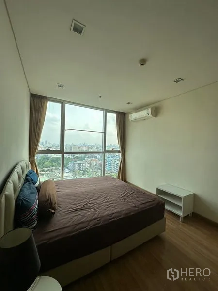 Condominium for sale in Watthana, Bangkok - Cozy bedroom with large bed, air conditioner and city view through full-height glass.