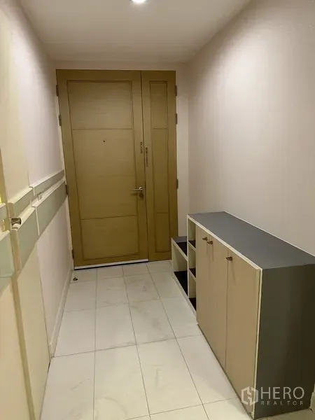 Condominium for rent in Watthana, Bangkok - Entrance hallway with wooden door, shoe cabinet and white tiled floor.