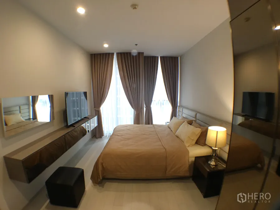 Condominium for rent in Pathum Wan, Bangkok - Cozy 1-bedroom master with king bed, TV wall, floor-to-ceiling curtains and soft lighting.