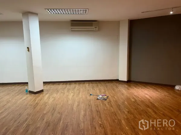 Office Space for rent in Khlong Toei, Bangkok - Corner of spacious workspace with a support column, wood-look flooring, gray accent wall and split-type air conditioner.
