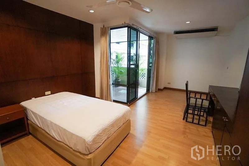 อพาร์ทเมนท์ ให้เช่าในWatthana, Bangkok - ห้องนอนพื้นไม้พร้อมโต๊ะทำงานและประตูกระจกบานเลื่อนไปยังระเบียงร่มรื่น