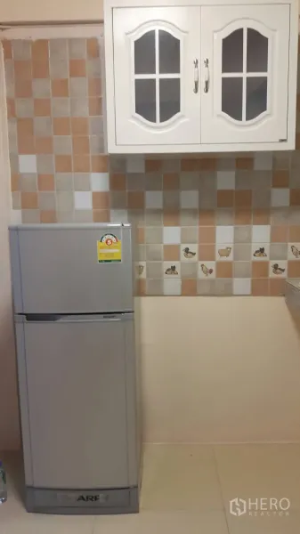 ทาวน์เฮาส์ ให้เช่าในKhlong Toei, Bangkok - ภาพระยะใกล้ของผนังกระเบื้อง ตู้ลอยสีขาว และตู้เย็นสีเงินในครัว