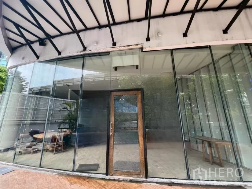 零售空间 出租 - 弧形落地玻璃门面与木质门，金属雨棚下的商铺入口，位于W District。