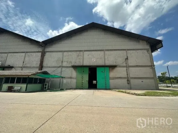 货栈 出租在Mueang Pathum Thani, Pathum Thani - 单体仓库立面，大型绿色推拉门，装卸坪与小型门卫亭。