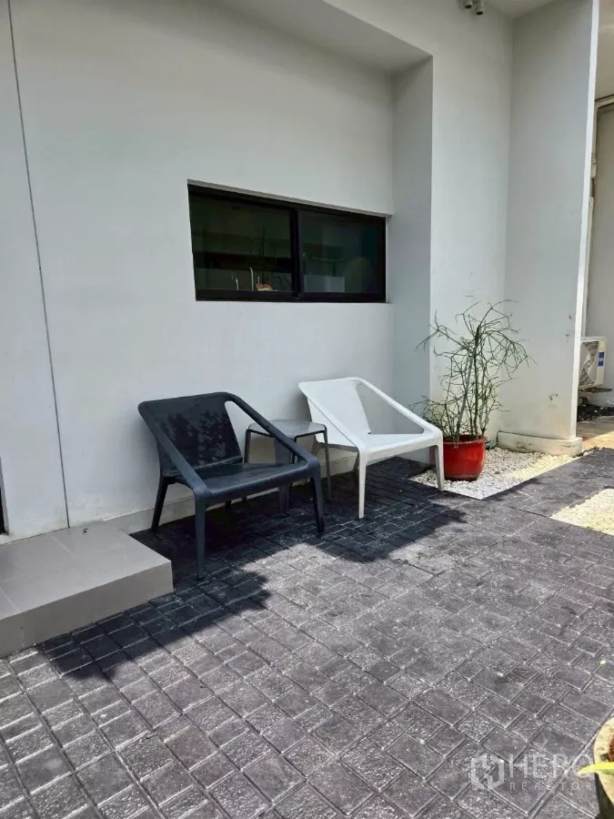 Townhouse for rent in Bang Phli, Samut Prakan - Small outdoor patio with two chairs, potted plant, and paved flooring against a white exterior wall.