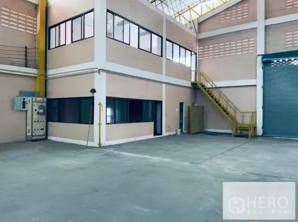 Warehouse for rent in Sam Phran, Nakhon Pathom - Interior with a two-storey glass-front office block, yellow metal stairs and an internal roller shutter door.
