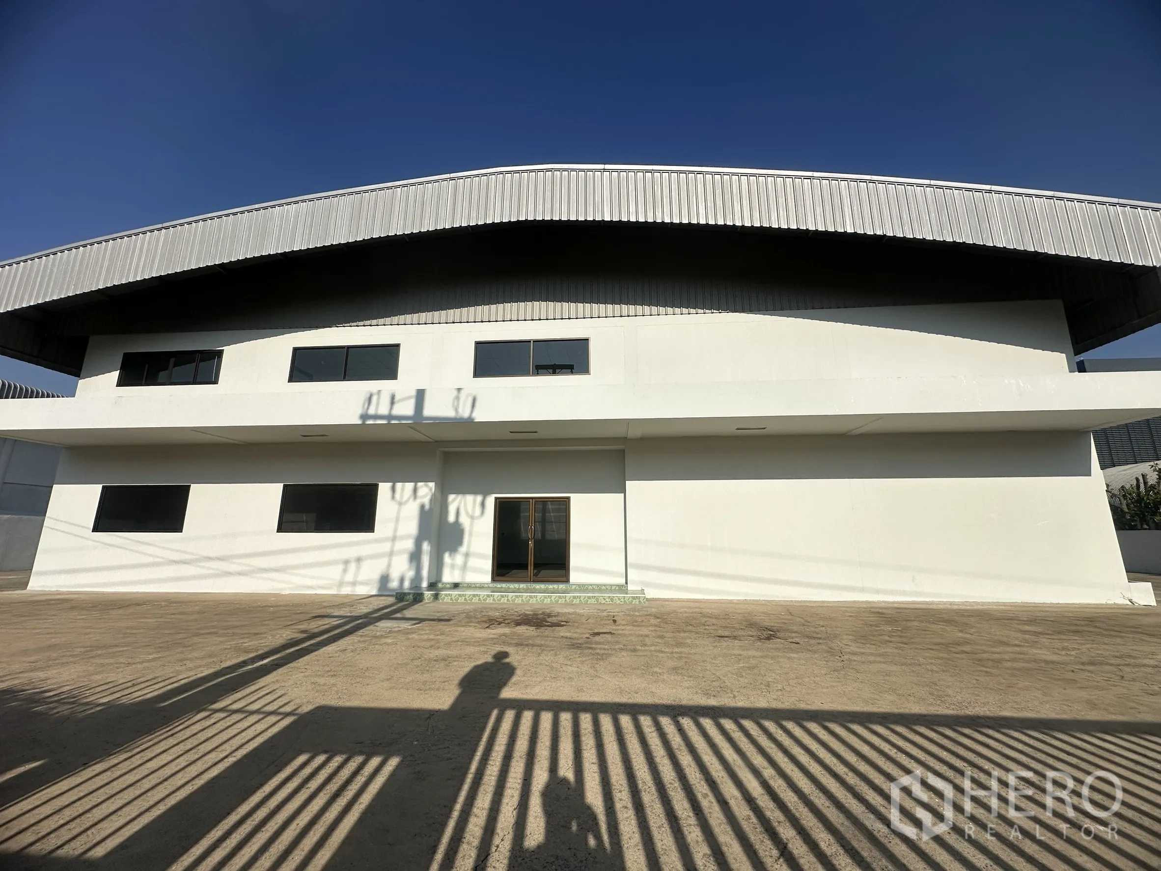 Factory for sale in Khlong Luang, Pathum Thani - Concrete yard in front of the facade with dark-framed windows.