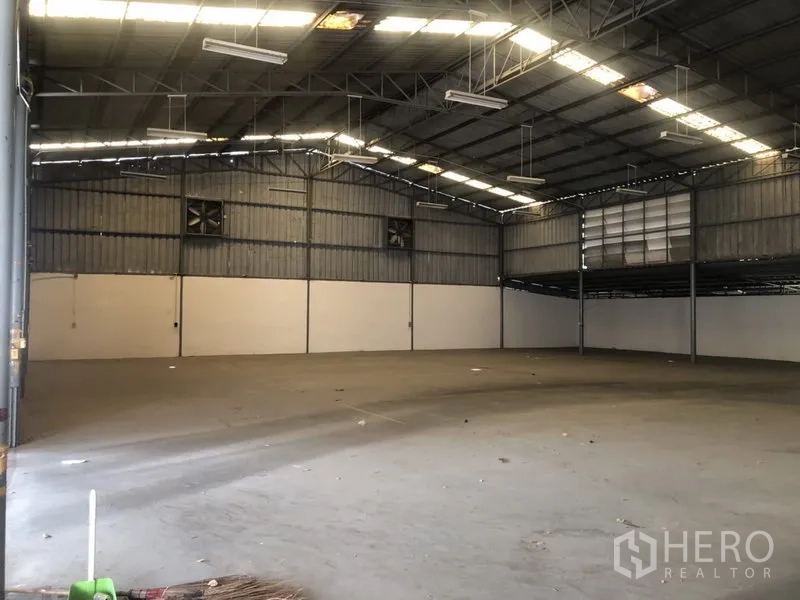 Warehouse for rent in Prawet, Bangkok - Spacious warehouse interior with high steel truss roof, skylights and ventilation fans.