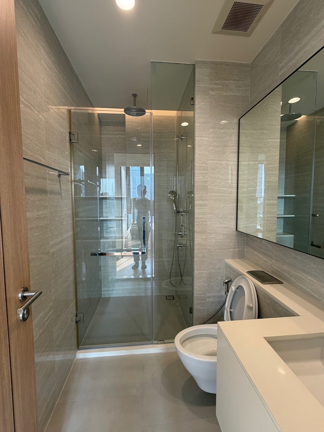 公寓 出租在Bang Rak, Bangkok - 现代卫浴，玻璃淋浴间配雨淋花洒，大镜面、悬空台盆与挂墙式马桶。