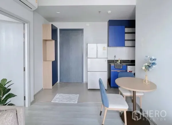 คอนโด ให้เช่าหรือขายในWatthana, Bangkok - มุมครัวสว่าง ตู้บิลท์อินสีฟ้า ตู้เย็นสีขาว และโต๊ะทานข้าวขนาดเล็กในคอนโดสมัยใหม่