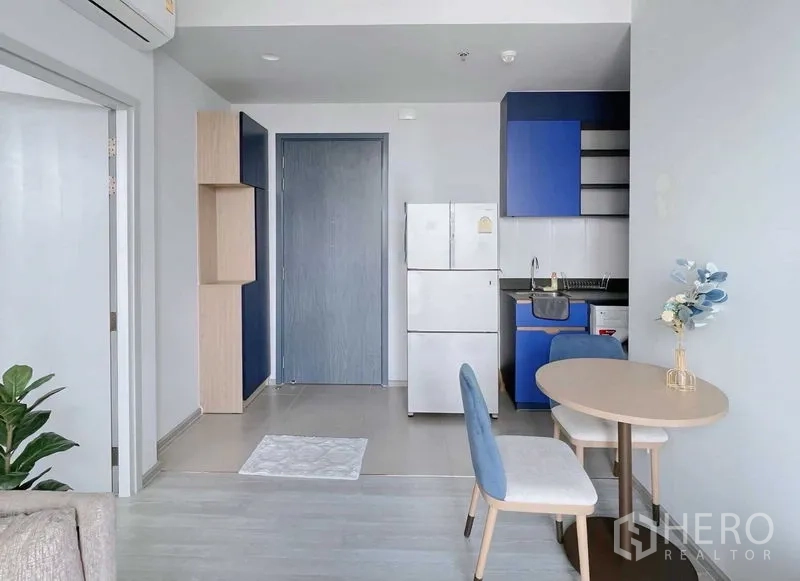คอนโด ให้เช่าหรือขายในWatthana, Bangkok - มุมครัวสว่าง ตู้บิลท์อินสีฟ้า ตู้เย็นสีขาว และโต๊ะทานข้าวขนาดเล็กในคอนโดสมัยใหม่