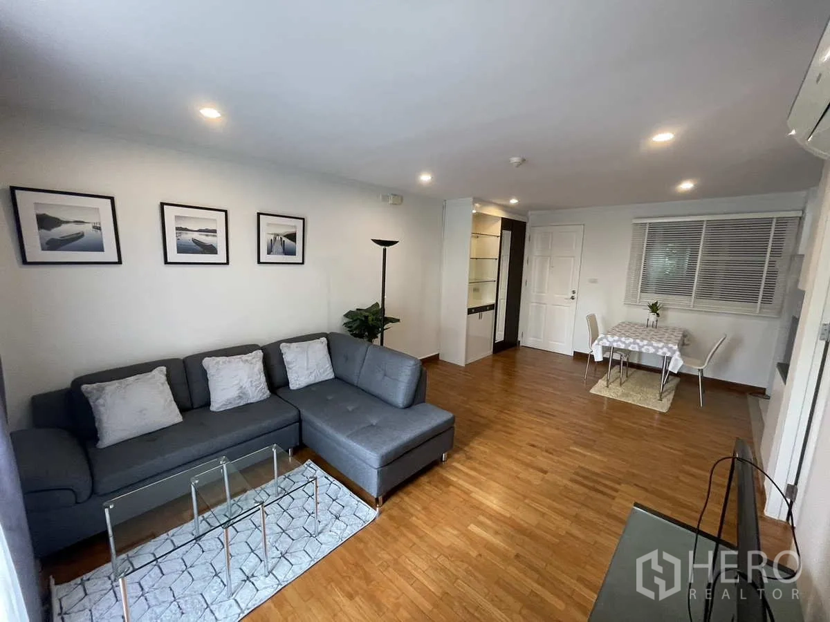 Condominium for rent in Watthana, Bangkok - Open-plan lounge with L-shaped sofa, wall art, dining nook and recessed lighting.