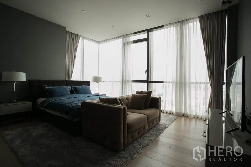Condominium for rent or sale in Watthana, Bangkok - Corner master bedroom with wraparound windows, sheer drapes and TV console.