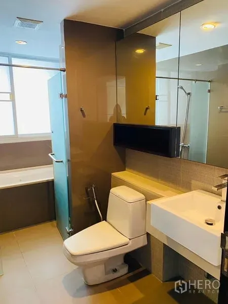 Condominium for rent in Watthana, Bangkok - Modern bathroom with bathtub, separate glass shower, large mirror, and contemporary fixtures.