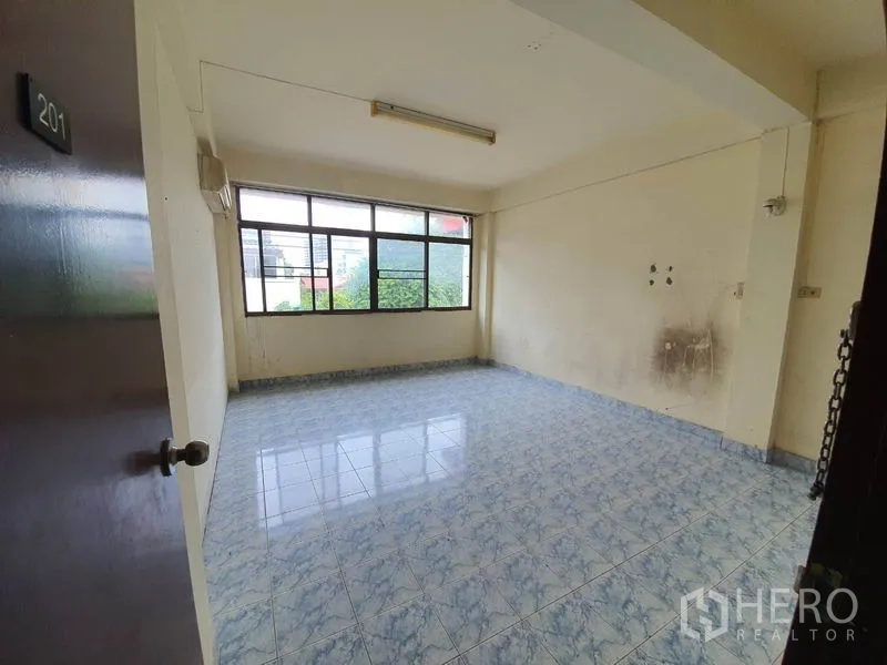 Shophouse for rent in Bang Rak, Bangkok - Room 201 featuring blue floor tiles, pale walls, and a wide window.