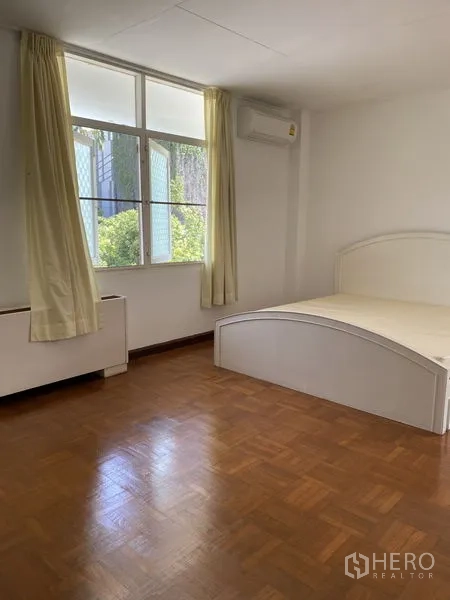 Apartment for rent in Khlong Toei, Bangkok - Bright master bedroom with large window, white bed frame, curtains and wood flooring.