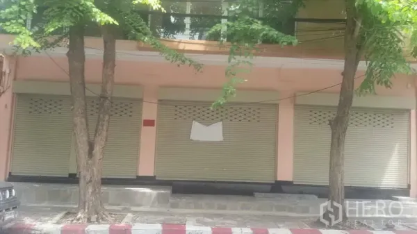 Office Space for rent in Sathon, Bangkok - Street-level building facade in Sathon with three beige roll-up shutters shaded by roadside trees.
