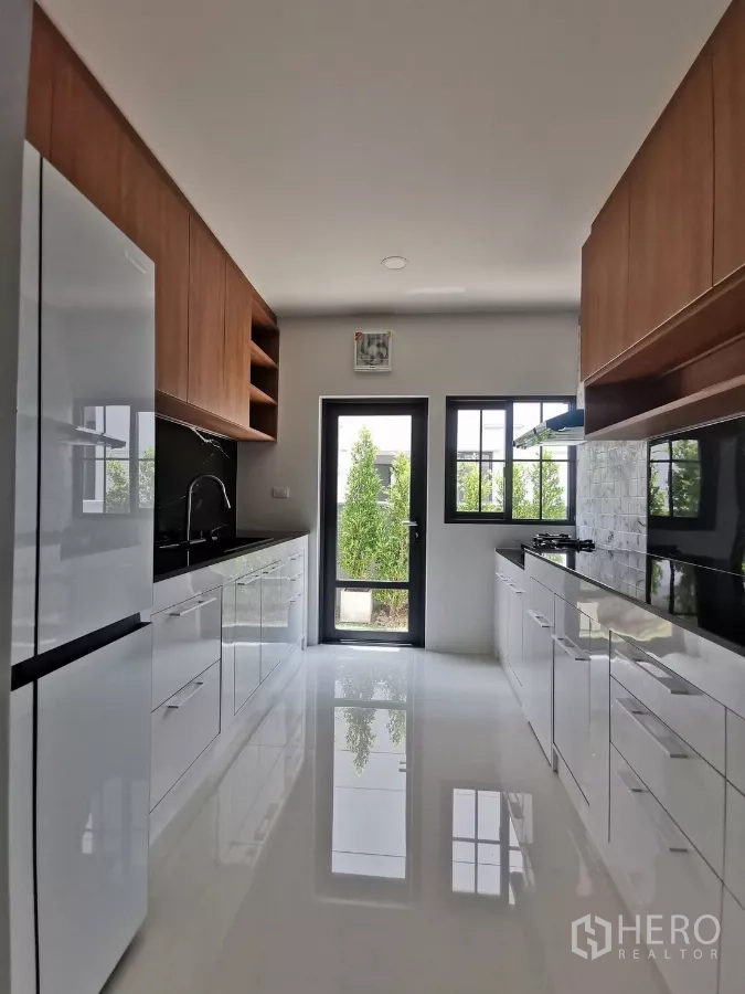 Detached House for rent in Bang Phli, Samut Prakan - Sleek galley kitchen with white cabinetry, black countertops and door to the garden.