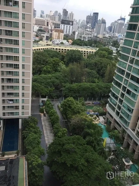 Condominium for rent in Pathum Wan, Bangkok - High-floor outlook between towers showing lush trees, a pool below and the Bangkok skyline.