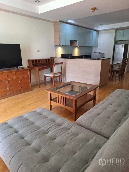 Apartment for rent in Watthana, Bangkok - Bright open-plan living room with gray sofa, TV console and wood floors facing a modern kitchenette.