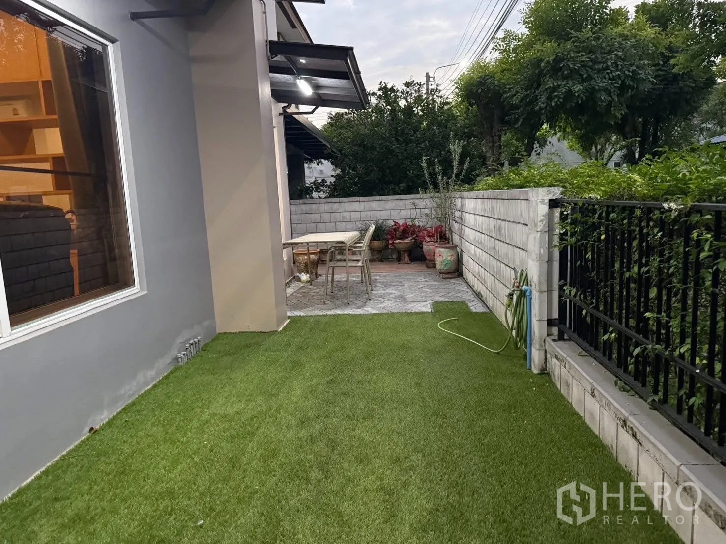 Detached House for rent in Bang Na, Bangkok - Side yard with artificial grass and a paved patio with outdoor dining set.